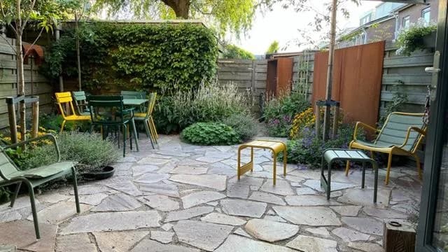 De stadstuin met een terras van flagstones, groene stoelen en borders