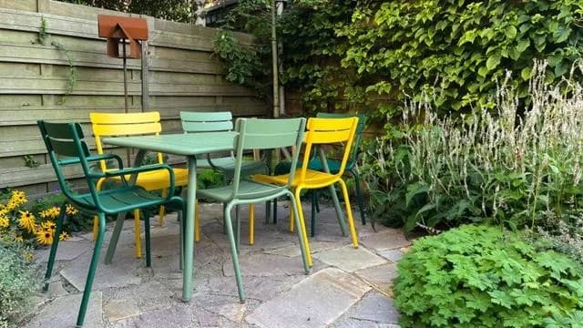 Groene en gele stoelen op het terras van flagstones tussen de borders