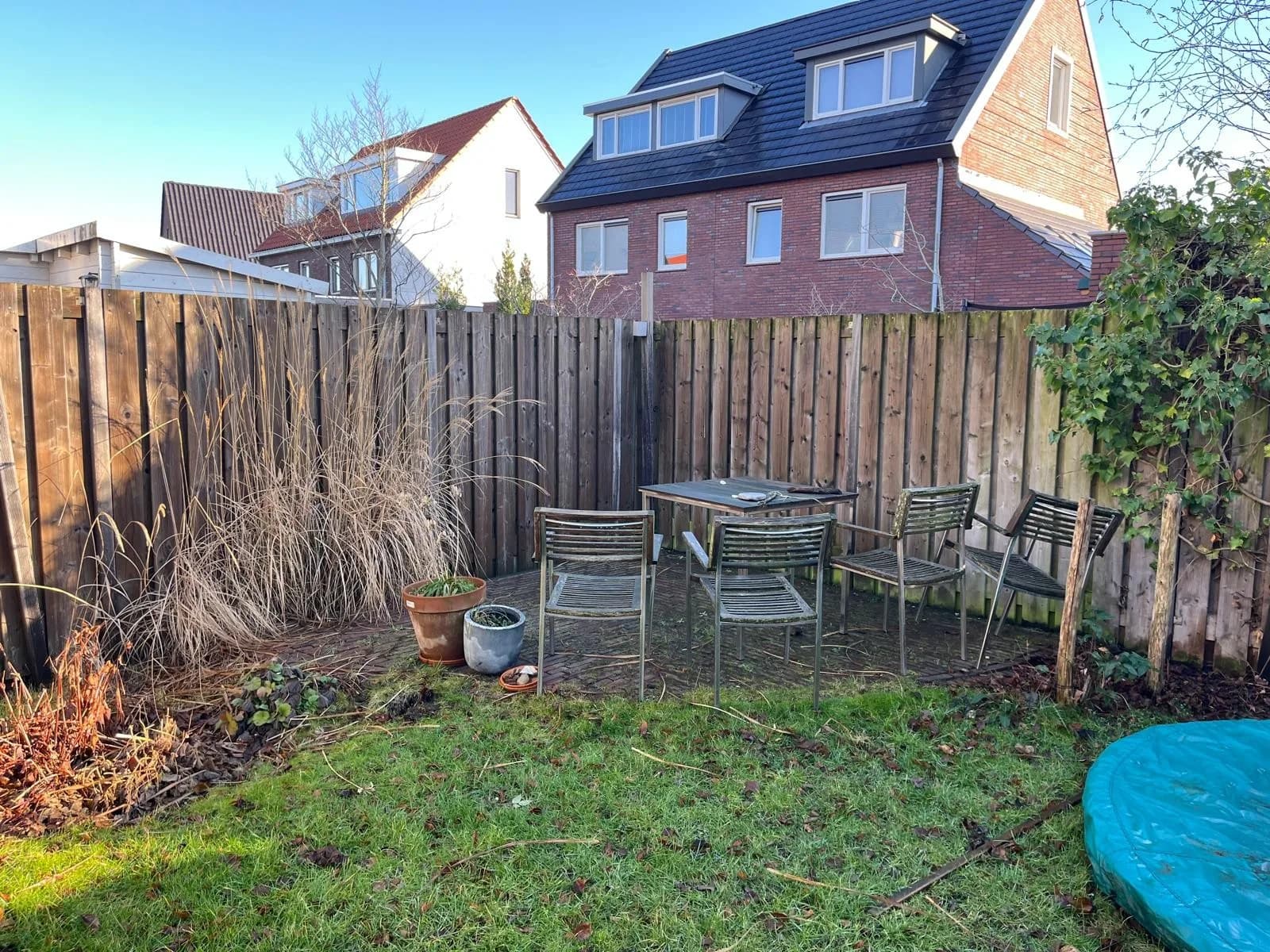 De achtertuin voor de aanleg, met gras en een losse zithoek bij de schutting