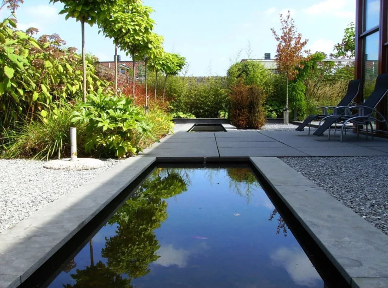 Strakke tuin met spiegelvijver onder de bomen in Den Haag