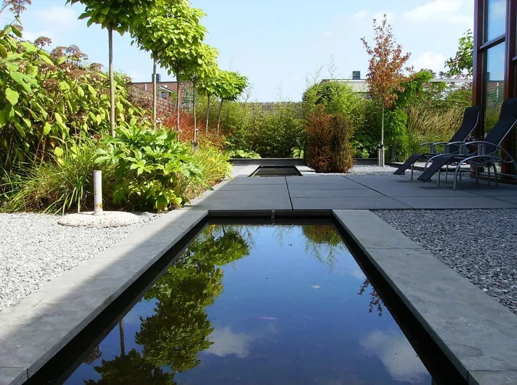 Strakke tuin met spiegelvijver onder de bomen in Den Haag