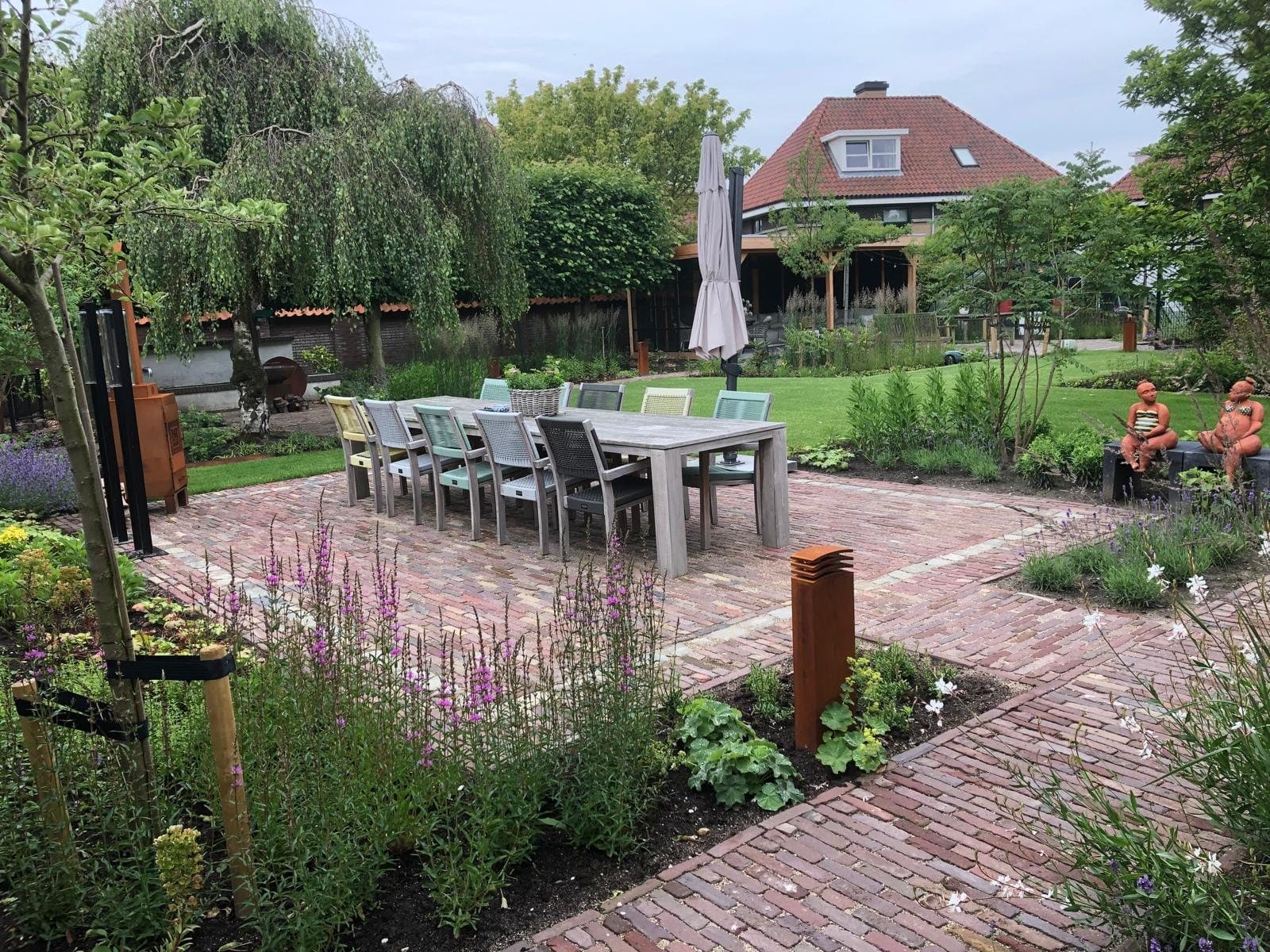 Terras van gebakken klinkers met bloeiende borders en een lange tafel, aangelegd door Diemel in Den Haag